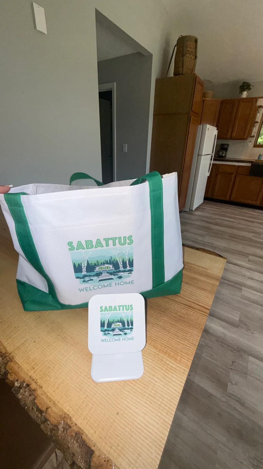 A green and white tote bag with "Sabbatus" on it sits on a wooden table.