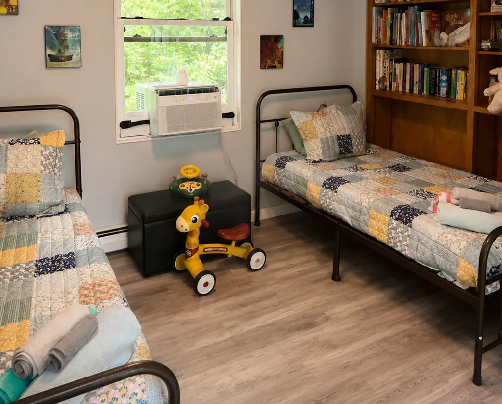 Two twin beds with quilts, a bookshelf, and a toy in a cozy room.