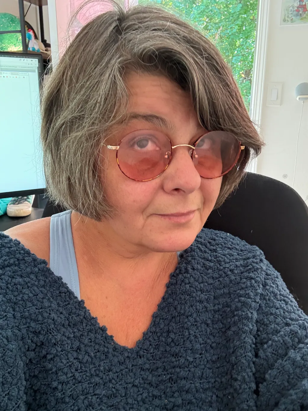 Woman with short gray hair wearing sunglasses and a blue sweater.
