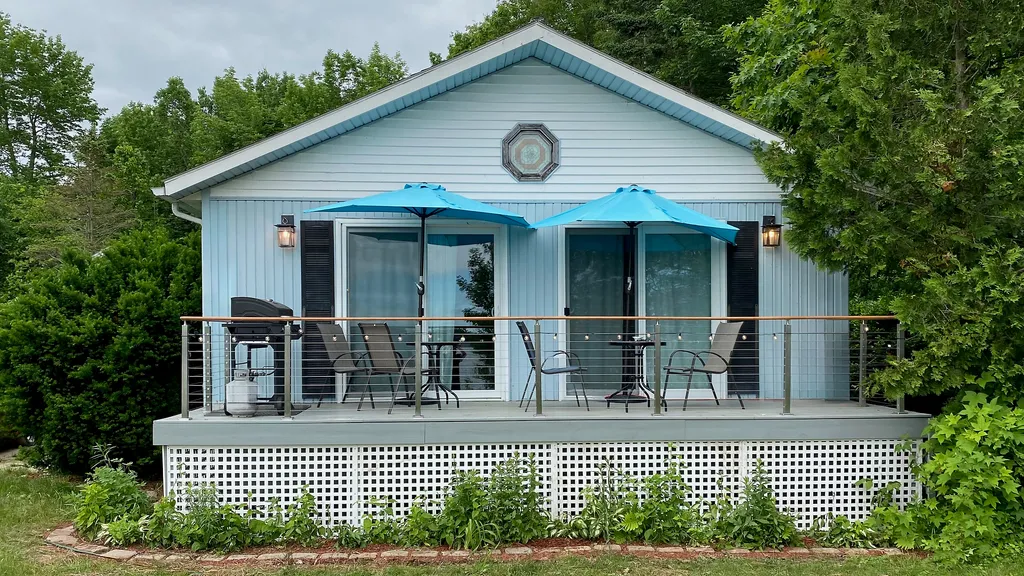 A blue cottage with a porch, two blue umbrellas, a grill, and a table.