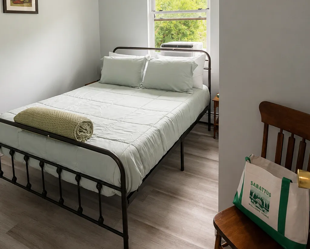 A bedroom with a bed, pillows, and a bag on a chair.