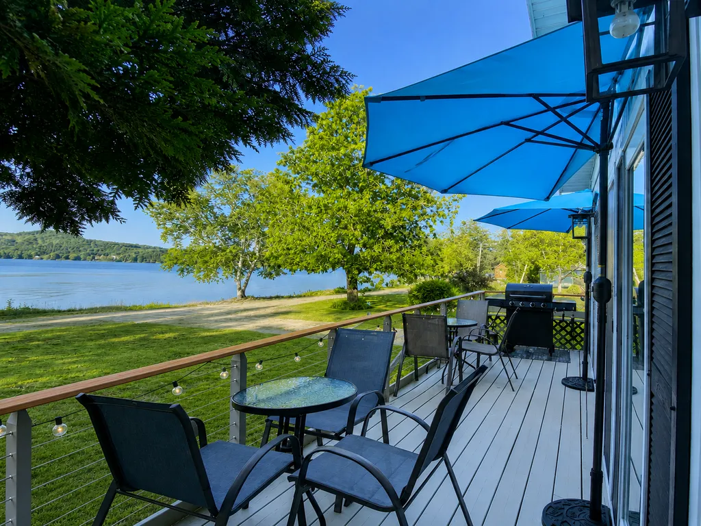 Deck with chairs, table, and blue umbrellas overlooking a lake.